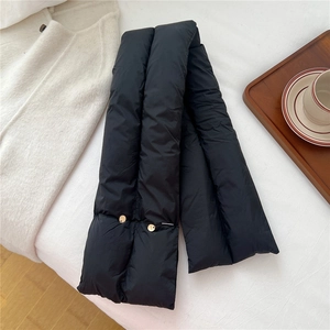 Detail of black puffer scarf with decorative gold buttons on a cozy white aesthetic background