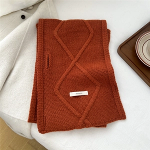 Detail of caramel orange wool knit scarf with diamond pattern and 100% wool label
