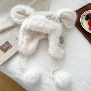Detail of plush cream earflap hat featuring thick faux fur texture and cute pom-pom ties
