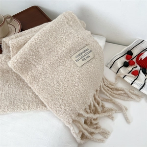 Close-up of beige bouclé knit scarf featuring soft texture and decorative fringe tassels