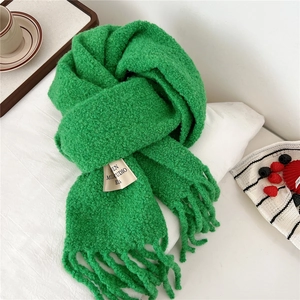 Detail view of a bright green knit scarf with thick tassels and a woven label on fabric