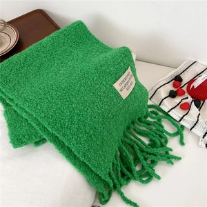 Detail of grass green knitted scarf featuring soft fringe and minimalist woven brand label