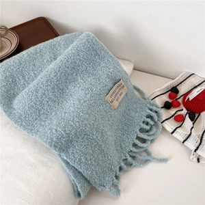 Close-up of light blue knit scarf texture with fringe detail and small woven label