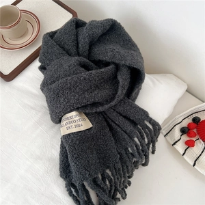 Detail of dark grey knit scarf with fringe and woven label on a cozy white background