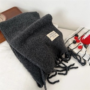 Detail of dark grey knit scarf with fringe and woven label on white fabric