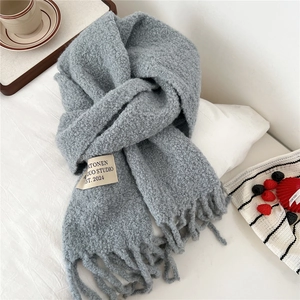Detail of grey thick knit scarf with long fringe and white brand label on bed