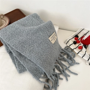 Detail of blue winter scarf showing soft fleece texture, long tassels, and woven label