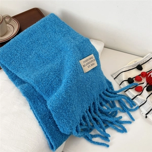 Detailed texture of thick blue knit scarf with soft tassels and woven logo label