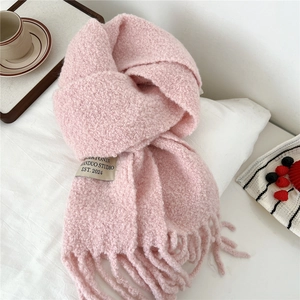 Detail of soft pink knitted scarf with decorative label and long tassels on white surface