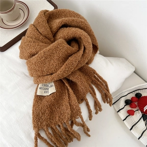 Detailed close-up of caramel textured knit scarf with tassels and stitched logo label