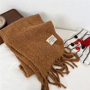 Macro detail of brown bouclé knit scarf with fringe and a minimalist brand label
