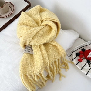 Macro view of cream yellow chunky knit scarf with long tassels on a white bed