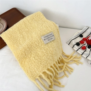 Detail of warm yellow knitted scarf with fuzzy texture, fringe edges and woven label