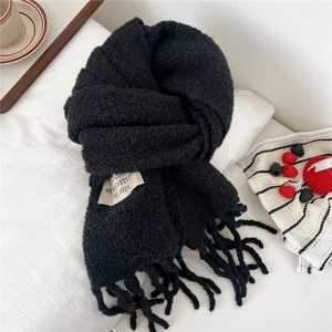 Detail of black thick knit scarf with fringe and minimalist woven label on white fabric