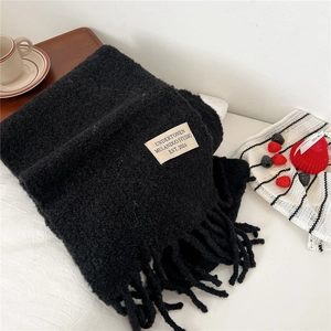 Close-up of thick black knit scarf with tassels and brand label on white bedding