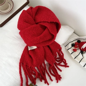 Detail shot of a vibrant red knitted scarf with tassels and white brand label on a cozy setup