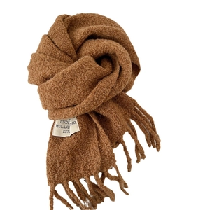 Thick caramel brown knit scarf with fringe and minimalist label on white background