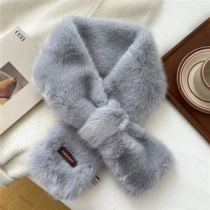 Detail of grey-purple faux fur cross-scarf with leather tag on a soft white blanket