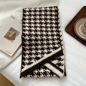 Detail of classic houndstooth knit scarf with soft texture on a cozy white blanket