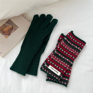 Close-up of winter knit gloves in forest green and colorful stripes on white fabric