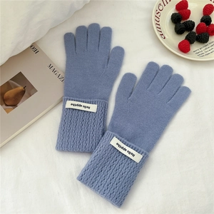 Détail des gants en tricot bleu brume avec poignets côtelés et écusson décoratif