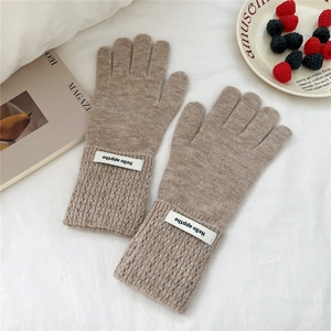 Détail de gants en maille beige avec poignets côtelés et étiquettes blanches décoratives