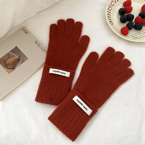 Détail de gants en maille rouge rouille avec étiquette blanche tissée au poignet
