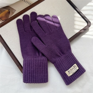 Dettaglio di guanti in maglia viola scuro con polsini a costine ed etichetta in tessuto