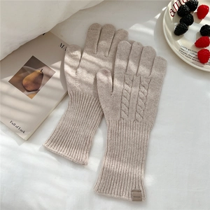 Detailed knit texture of beige wool gloves with twist pattern and leather tag
