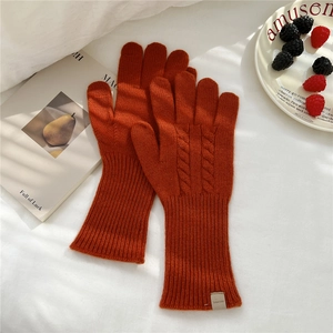 Close-up of caramel orange cable knit wool gloves with ribbed cuffs on white linen fabric