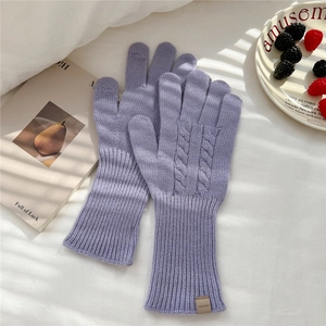 Close-up of lavender cable knit gloves with wool label and long ribbed cuffs on bed