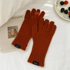 Close-up of rust red wool knitted gloves featuring elegant braided texture and logo tag