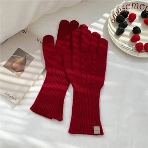 Close-up of red cable knit gloves with ribbed cuffs on a white bed sheet backdrop