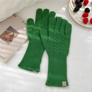 Detail view of grass green wool knit gloves with cable pattern and 100% wool material tag