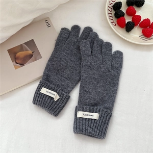 Detail of dark grey 100% wool knitted glove cuff with white woven label on cozy background
