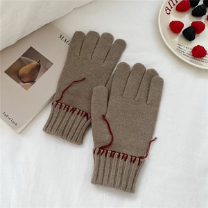 Close-up of thick knitted gloves with red stitching detail and minimalist texture