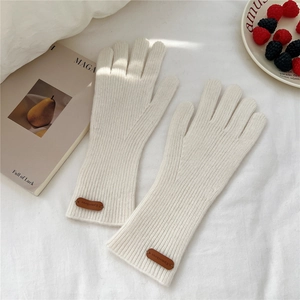 Détail de gants en tricot beige chaud avec logo en cuir sur les poignets côtelés