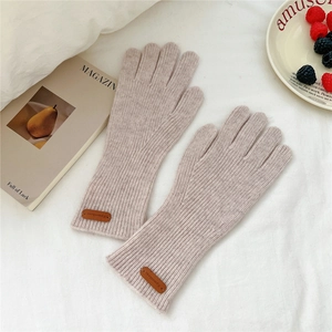 Détail de gants en tricot beige-rose avec texture côtelée et écusson en cuir marron