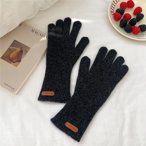 Détail de gants en tricot gris foncé avec écusson en cuir sur tissu blanc doux