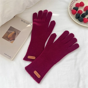 Détail de gants en tricot bordeaux avec logo en cuir et poignets longs côtelés