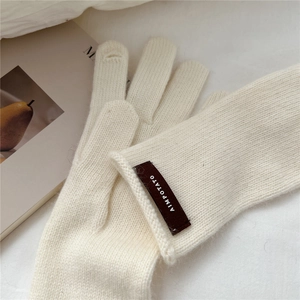 Close-up of cream knit gloves with leather logo patch and touchscreen thumb opening