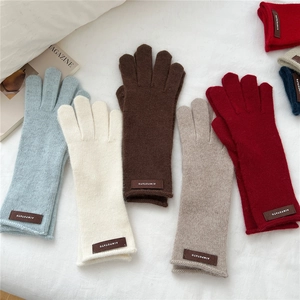 Knitted winter gloves in multiple colors with leather tag on a soft white background