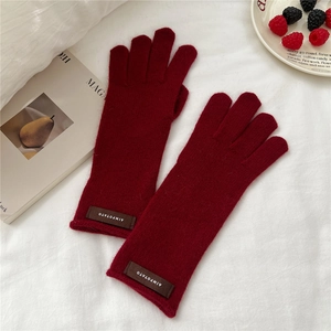 Detail of dark red knit glove featuring a leather brand tag and soft cashmere texture