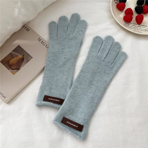 Detail of light blue knitted glove with a brown leather logo patch on white fabric