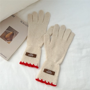 Detail of cream knit gloves with red scalloped trim and brown leather handmade label
