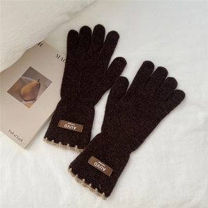 Detail of dark brown knit gloves with beige scalloped cuffs and leather brand label