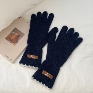 Detail of dark blue knit gloves with brown leather tag and grey crochet lace trim
