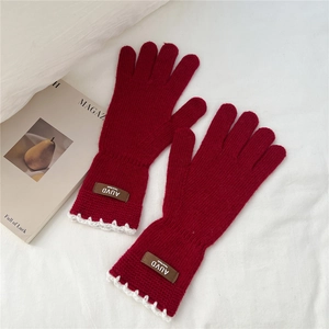 Close-up of red knit gloves featuring scalloped white lace trim and handmade leather label
