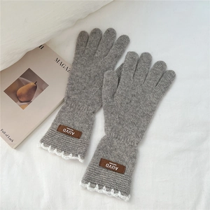 Detailed texture of grey knitted gloves with white lace trim and premium leather patch