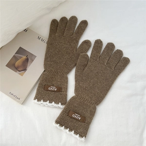 Close-up of brown knit gloves featuring white lace trim and handmade leather label